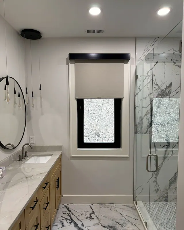 Roller shade with a black cassette on a bathroom window beside a glass shower