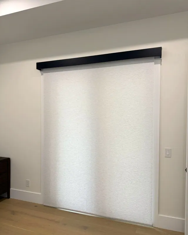 One wide light filtering roller shade lowered over a patio door