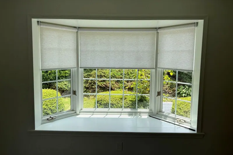 Light filtering roller shades half lowered across a bay window
