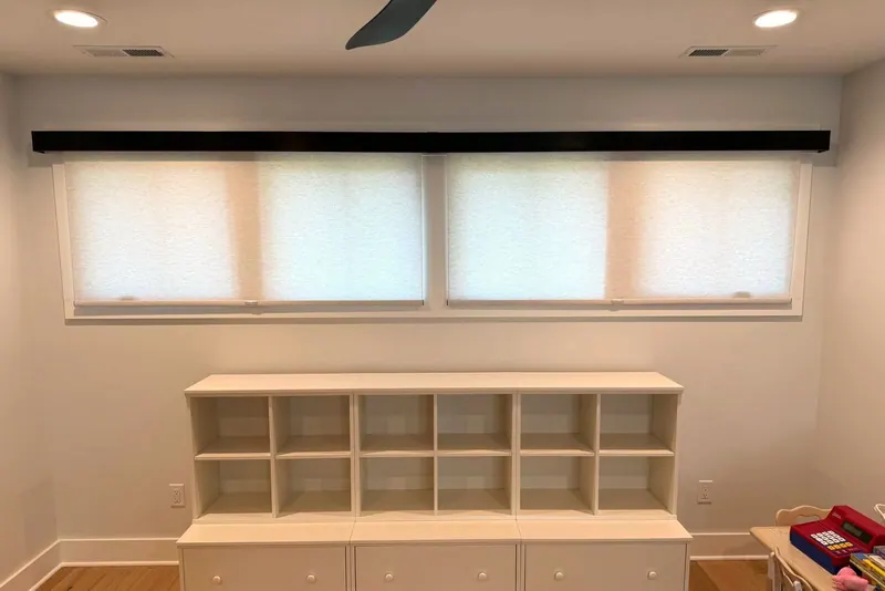 Four roller shades under one valance above a built-in bookcase
